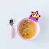 Bumkins Silicone Grip Bowl: Pink holds soup with rice, while a star-shaped cup of crackers and a pink spoon sit nearby on a white background.
