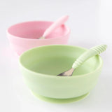 Bumkins Silicone Grip Bowl: Sage with a matching spoon on a white background, with a pink bowl and spoon blurred behind.