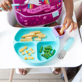 A child in a high chair enjoys green beans, cheese hearts, and crinkle-cut fries with ketchup from a Bumkins Silicone Grip Dish: Blue.