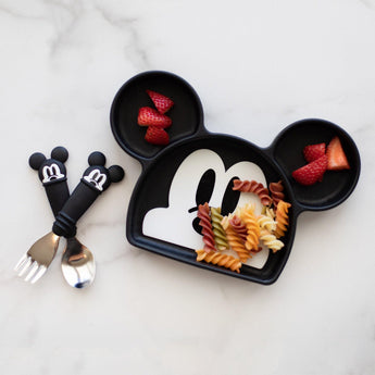 Bumkins Silicone Grip Dish: Mickey Mouse with pasta and strawberries, plus matching utensils on a marble surface.