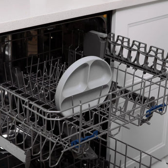 Bumkins Silicone Grip Dish: Gray sits in the top rack of an open dishwasher.