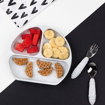 Bumkins Silicone Grip Dish: Gray holds fruit and waffles, with utensils on a black & white background with a heart print pouch nearby.