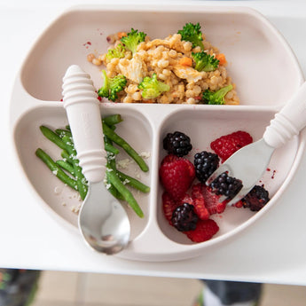 Close-up of Bumkins Silicone Grip Dish: Sand with couscous, broccoli, green beans, and berries, alongside a spoon and fork.