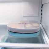 A Bumkins Silicone Grip Dish, gray with a leak-resistant lid, sits on a refrigerators glass shelf.