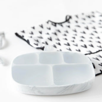 Bumkins Silicone Grip Dish with Lid (5 Section): Marble sits on a white background with a heart-patterned bib blurred behind.