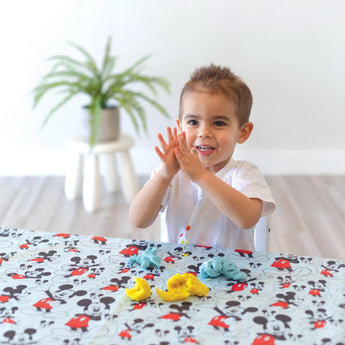 A child molds clay on a table covered by a splat mat from Bumkins Disney Little Ones Gift Bundle: Mickey Mouse Classic.