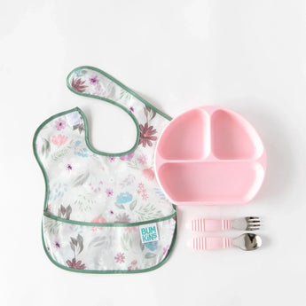 A floral bib, pink divided plate, and pink utensils from Bumkins Ultimate Gift Set - Floral & Lace on a white background.