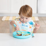 A toddler in an ocean-themed bib eats from a blue plate with a fork, all from Bumkins Ultimate Gift Set - Ocean Life & Whale Tail.