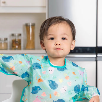 A toddler wears a ocean-themed bib from Bumkins Ultimate Gift Set - Ocean Life & Whale Tail in a bright kitchen.