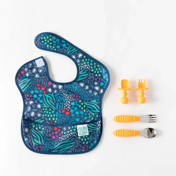 A dark blue bib sits next to two sets of orange utensils from Bumkins Ultimate Gift Set - Jungle & Animal Prints on a white background.