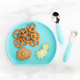 Bumkins Silicone Grip Plate: Blue holds pretzels, peanut butter, and cucumber slices on a marble background, with blue utensils nearby.