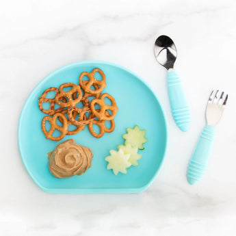 Bumkins Silicone Grip Plate: Blue holds pretzels, peanut butter, and cucumber slices on a marble background, with blue utensils nearby.