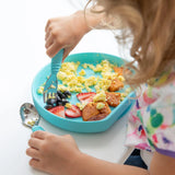 A child enjoying eggs, berries & sweet potatoes with a fork from a Bumkins Silicone Grip Plate: Blue on a white table.