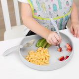 Close-up of a child enjoying macaroni, strawberries, & avocado with a fork from Bumkins Silicone Grip Plate: Gray on a white table.