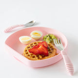 Bumkins Silicone Grip Plate: Pink holds waffles, strawberries, eggs, and kiwi beside pink utensils on a white background.