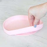 A hand holds a Bumkins Silicone Grip Plate: Pink, demonstrating the suction cup bottom on a marble surface.