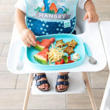 A toddler in a high chair enjoys a meal from a Bumkins Silicone Grip Tray: Blue, featuring watermelon, noodles, and star-shaped treats.