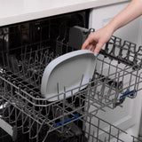 A hand places a Bumkins Silicone Grip Tray: Gray into the top rack of an open dishwasher.