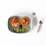 Bumkins Silicone Grip Tray: Gray holds two mini pizzas, garnished with kiwi slices and a blackberry on a white background next to utensils.