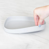 A hand holds a Bumkins Silicone Grip Tray: Gray, demonstrating the suction cup bottom on a marble surface.