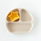 A yellow Bumkins Silicone Little Dipper 3-Pack: Tutti-Frutti sits in a sectioned beige plate on a white background.
