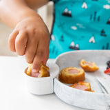 Close-up of a child in blue bib dipping corn dogs into sauce in a marble Bumkins Silicone Little Dipper Round 3-Pack: Taffy.