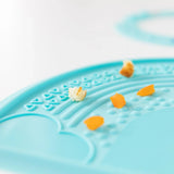 Close-up of Bumkins Silicone Sensory Placemat: Blue on a white background with food bits scattered on top.