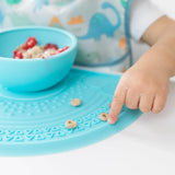 Close-up of a child's hand reaching for cereal pieces on a Bumkins Silicone Sensory Placemat: Blue with a blue bowl on top.