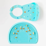 Bumkins Silicone Sensory Placemat: Blue covered with fruit pieces lays on a white background, with a blue silicone bib sitting above.