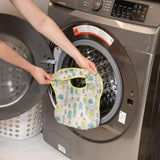A person holds Bumkins SuperBib®: Cacti in front of an open front-loading washing machine.