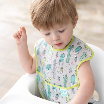 A young child in a high chair wears a Bumkins SuperBib®: Cacti.