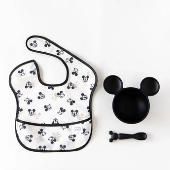 A Bumkins SuperBib® 3 Pack: Love, Mickey lays flat on a white background next to a black Mickey-shaped bowl and spoon set.