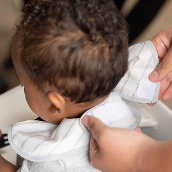 Adult hands adjust the hook-and-loop closure of a Bumkins SuperBib® 3 Pack: Love, Mickey around a child's neck.