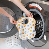 A person holds a Bumkins SuperBib® 3 Pack: Pooh Bear and Friends in front of a front-loading washing machine.