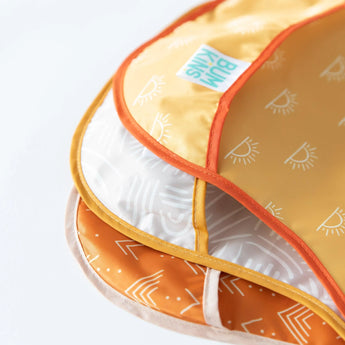Close-up of Bumkins SuperBib® 3 Pack: Desert Boho stacked on a white background, with focus on the catch-all pocket.