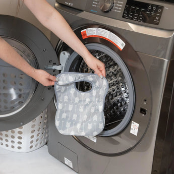 A person holds Bumkins SuperBib®: Arrow in front of an open front-loading washing machine.