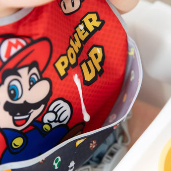 Close-up of a child wearing a red Bumkins SuperBib® 3 Pack: Super Mario™ Power-Up, with focus on yogurt dripping into the pocket.