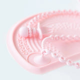 Close-up of a Bumkins Silicone Accessory Tether 2-Pack: Pink attached to a pink placemat on a white background, holding a toddler utensil.