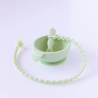 A Bumkins Silicone Accessory Tether 2-Pack: Sage is attached to a green spoon in a green bowl on a white background.