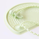 Close-up of a Bumkins Silicone Accessory Tether 2-Pack: Sage with a silicone placemat and fork on a white background.