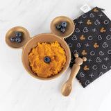 Bumkins Silicone First Feeding Set: Minnie Mouse Gold holds sweet potatoes and blueberries near a black printed pouch on a marble surface.