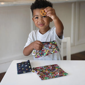 A child holds a pretzel at a white table with Bumkins Reusable Snack Bag, 3-Pack: Super Mario™ Power Up.