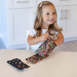 A girl with long hair sits at a white table, holding a Bumkins Reusable Snack Bag, 3-Pack: Super Mario™ Power Up.