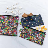 Bumkins Reusable Snack Bag, 3-Pack: Super Mario™ Power Up lays on a marble surface with snacks like popcorn, cookies, and cheese cubes.