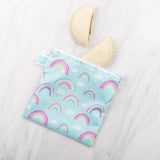 Two crustless sandwich halves spill from a blue Bumkins Reusable Snack Bag, Large 2-Pack: Rainbows & Unicorns on a marble surface.