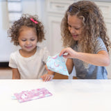 Two curly-haired girls smile as they open Bumkins Reusable Snack Bag, Small 2-Pack: Rainbows & Unicorns at a white table.