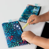 Close-up of a child holding a snack near Bumkins Reusable Snack Bag, Small 2-Pack: Jungle & Animal Prints on a white table.