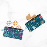 Bumkins Reusable Snack Bag, Small 2-Pack: Jungle & Animal Prints, filled with pretzels and cookies, rests on a marble background.