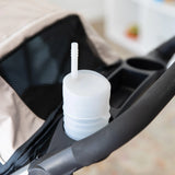 A Bumkins Silicone Straw Cup with Lid: Gray sits in the cup holder of a stroller.