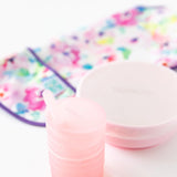 Bumkins Silicone Straw Cup with Lid: Pink sits on a white background, with a pink bowl and floral bib blurred behind.